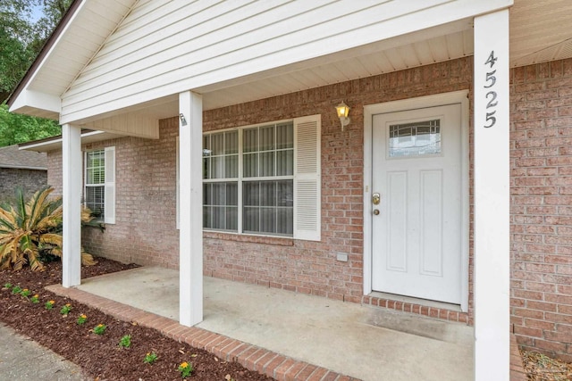 doorway to property featuring covered porch and brick siding
