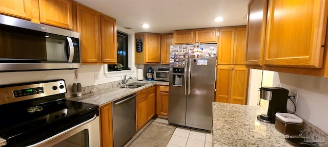 kitchen with stainless steel appliances, brown cabinetry, a sink, and light stone counters