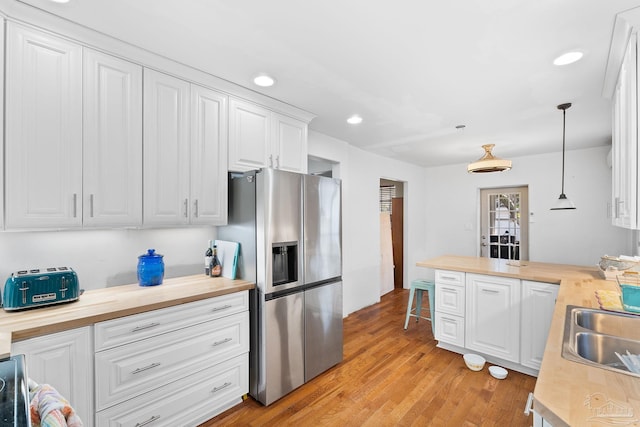 kitchen featuring hanging light fixtures, butcher block counters, stainless steel fridge, light hardwood / wood-style floors, and white cabinetry