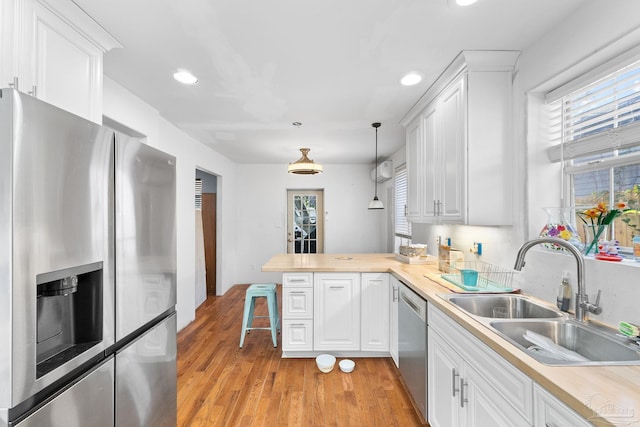 kitchen with sink, white cabinetry, kitchen peninsula, hanging light fixtures, and appliances with stainless steel finishes