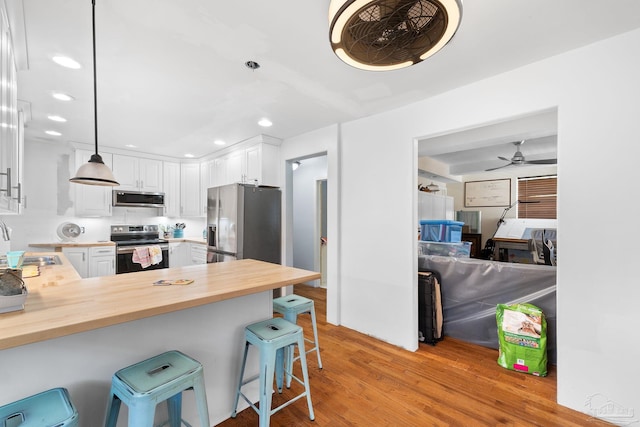 kitchen with stainless steel appliances, kitchen peninsula, ceiling fan, a breakfast bar, and white cabinets