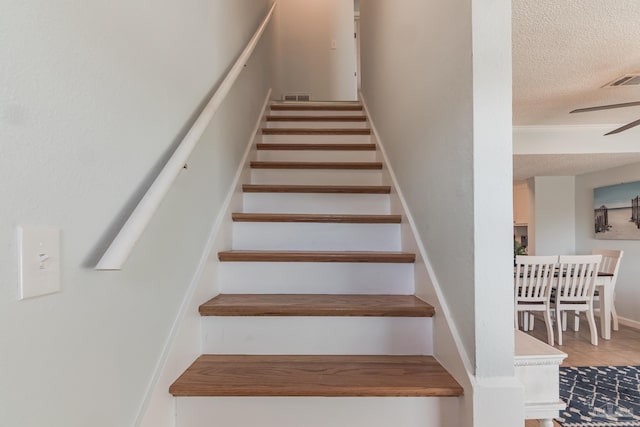 staircase with ceiling fan and a textured ceiling