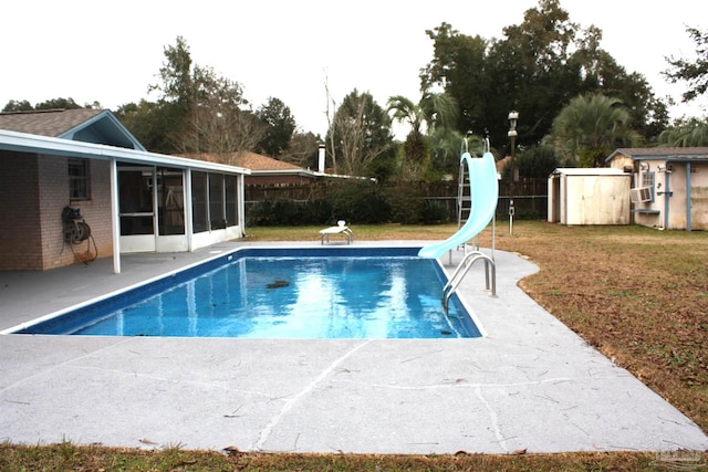 view of pool featuring a sunroom, a diving board, a water slide, a shed, and a patio