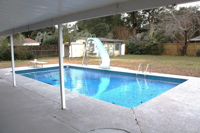 view of pool featuring a lawn, a water slide, a diving board, a patio area, and a storage unit