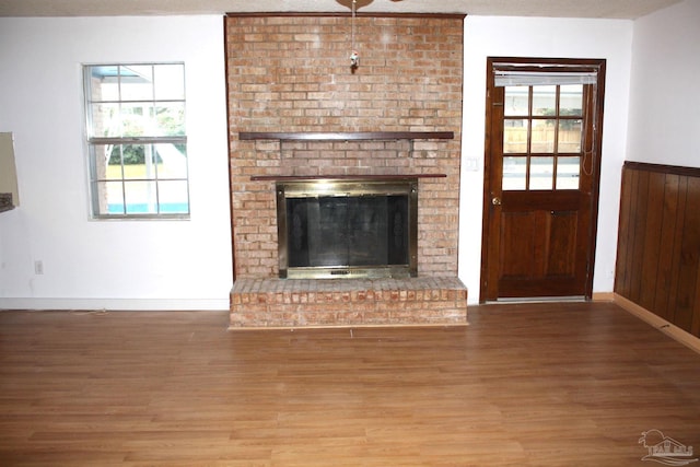 unfurnished living room with hardwood / wood-style floors, a brick fireplace, and wood walls