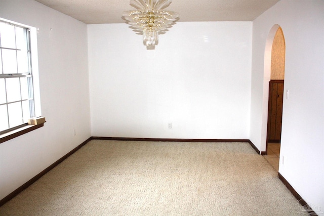 carpeted empty room with a notable chandelier and a wealth of natural light