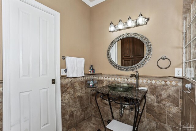 bathroom with tiled shower, tile walls, a sink, and a wainscoted wall