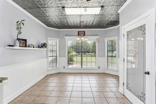 interior space featuring crown molding, an ornate ceiling, a notable chandelier, and a wainscoted wall