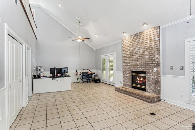 unfurnished living room featuring crown molding, wainscoting, a brick fireplace, a ceiling fan, and light tile patterned floors