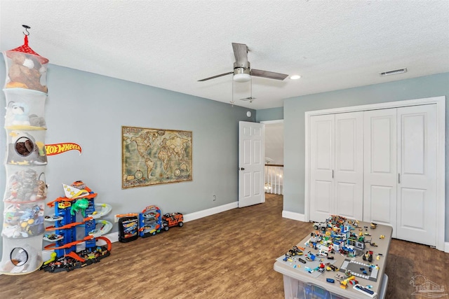recreation room with a textured ceiling, a ceiling fan, baseboards, wood finished floors, and visible vents