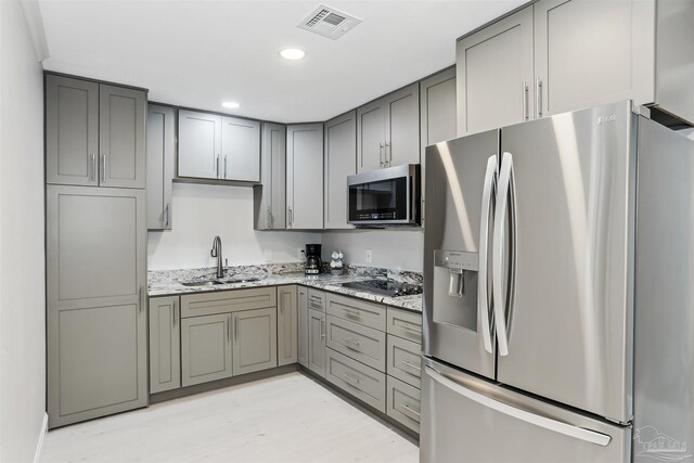 kitchen featuring a sink, gray cabinets, appliances with stainless steel finishes, and light stone countertops
