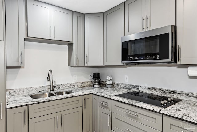 kitchen featuring light stone countertops, a sink, black electric cooktop, stainless steel microwave, and gray cabinetry