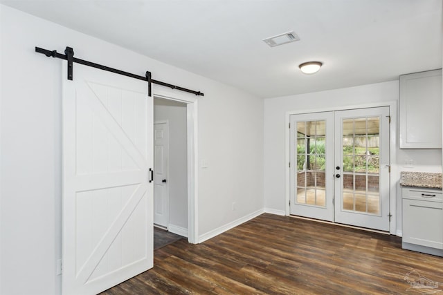 interior space with a barn door, french doors, and dark wood-type flooring