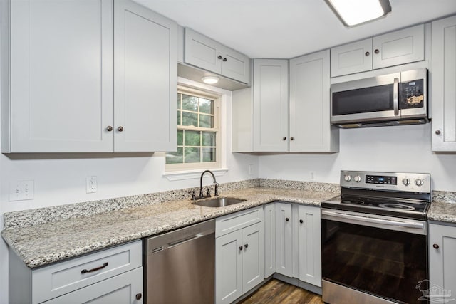 kitchen with light stone counters, dark hardwood / wood-style flooring, sink, and appliances with stainless steel finishes