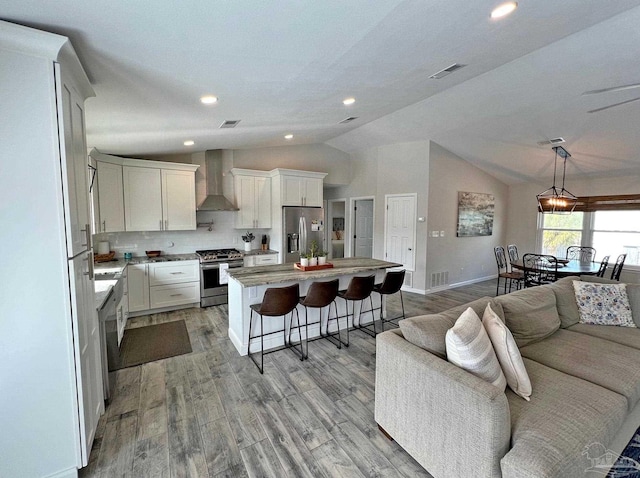 kitchen featuring stainless steel appliances, wall chimney range hood, a kitchen island, vaulted ceiling, and white cabinets