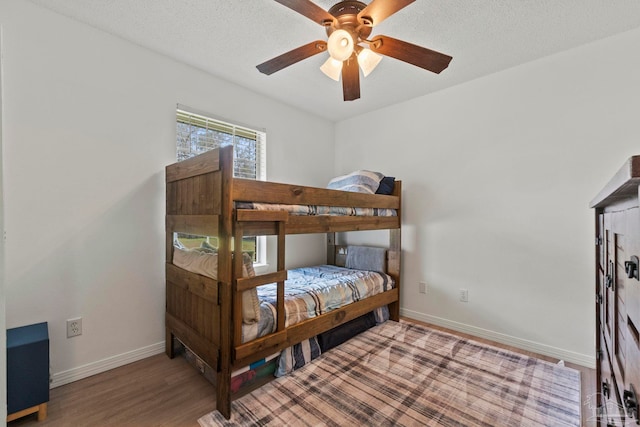 bedroom featuring a ceiling fan, a textured ceiling, baseboards, and wood finished floors