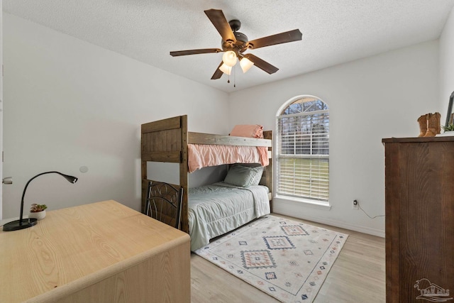 bedroom featuring a textured ceiling, baseboards, a ceiling fan, and light wood-style floors