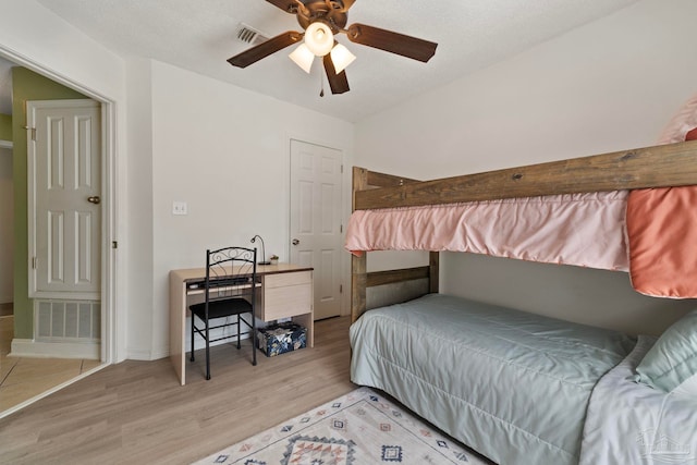 bedroom featuring light wood-style floors, a ceiling fan, visible vents, and a textured ceiling