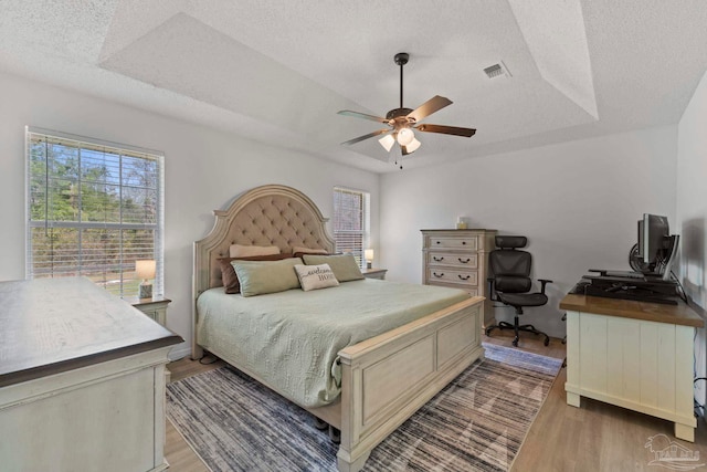 bedroom with a textured ceiling, a raised ceiling, visible vents, and light wood-style floors