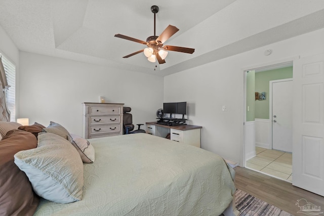 bedroom featuring a ceiling fan, a textured ceiling, a tray ceiling, and wood finished floors