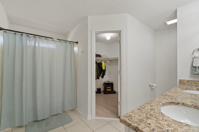 bathroom with a textured ceiling, a sink, a spacious closet, tile patterned floors, and double vanity