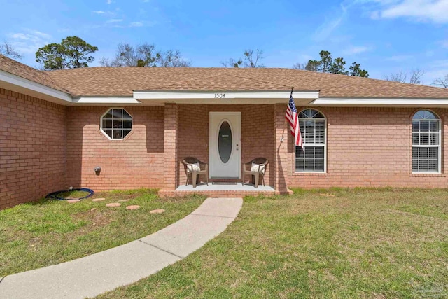 entrance to property featuring brick siding, a lawn, and roof with shingles