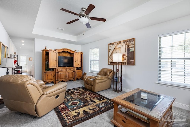 living room featuring ceiling fan, a healthy amount of sunlight, a raised ceiling, and light colored carpet