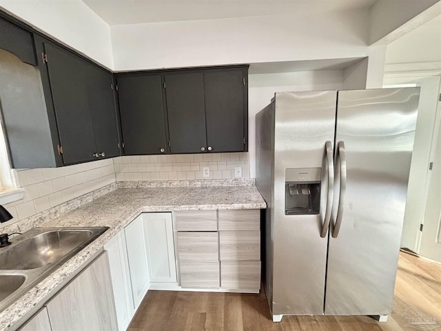 kitchen with a sink, backsplash, wood finished floors, and stainless steel fridge with ice dispenser