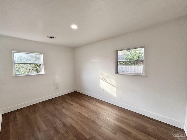 empty room featuring visible vents, baseboards, a healthy amount of sunlight, and dark wood-style flooring