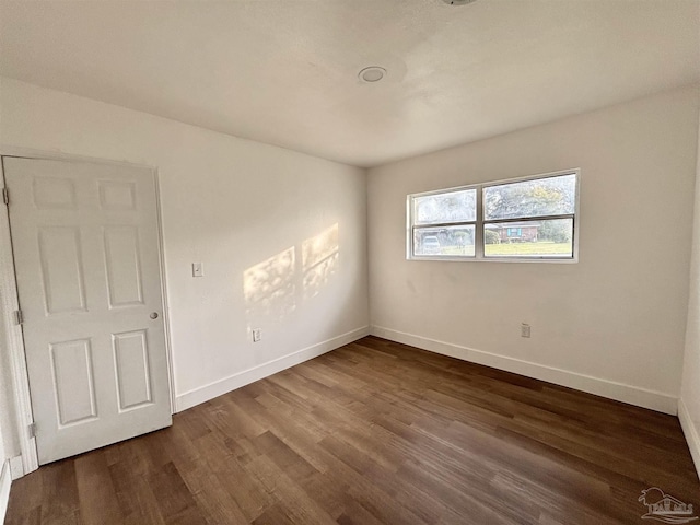 spare room with baseboards and dark wood-style floors