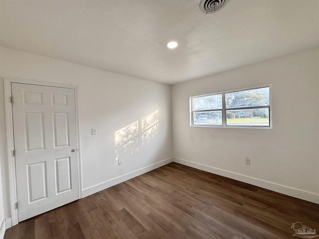 spare room featuring dark wood-style floors, visible vents, and baseboards