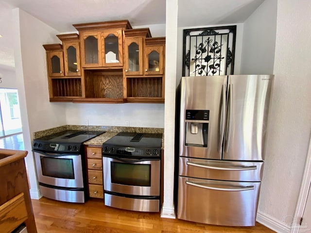 7208 Bayshore Dr, Milton, FL 32583 - kitchen featuring appliances with stainless steel finishes, light wood-type flooring, glass insert cabinets, and brown cabinets