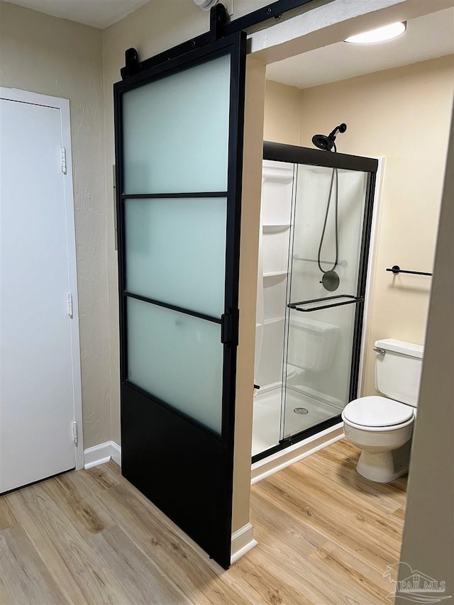 bathroom featuring hardwood / wood-style flooring, a shower with shower door, and toilet