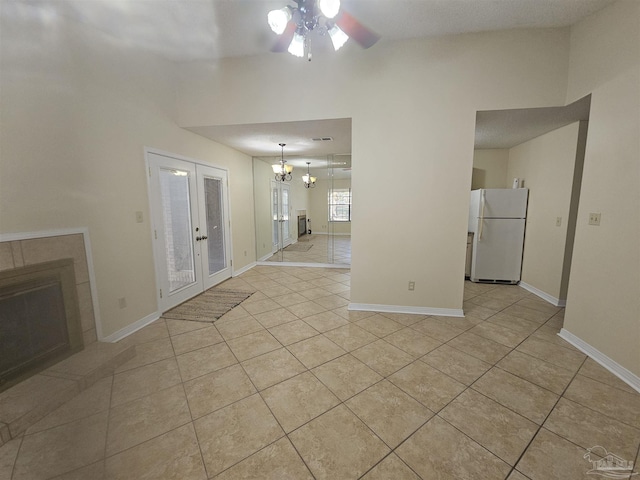 unfurnished living room featuring ceiling fan with notable chandelier, light tile patterned floors, a fireplace, and french doors