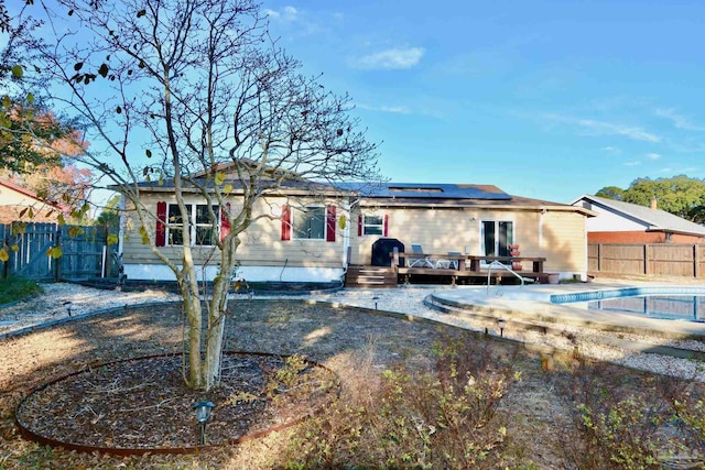 back of property with solar panels and a swimming pool side deck