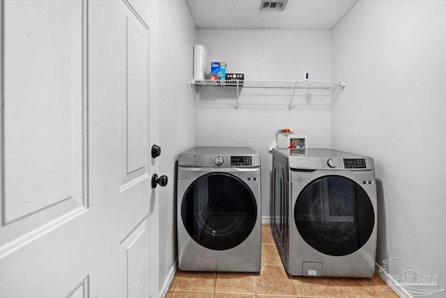 washroom featuring a textured ceiling, washing machine and dryer, and light tile patterned floors