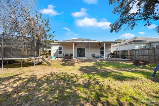 back of property with a yard, a trampoline, a fire pit, a patio, and ceiling fan