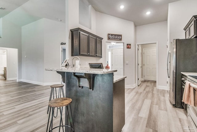 kitchen with light wood-type flooring, a towering ceiling, dark brown cabinetry, and a breakfast bar