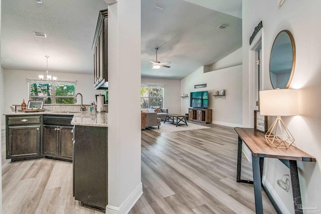 kitchen with light hardwood / wood-style floors, light stone countertops, dark brown cabinetry, vaulted ceiling, and ceiling fan with notable chandelier