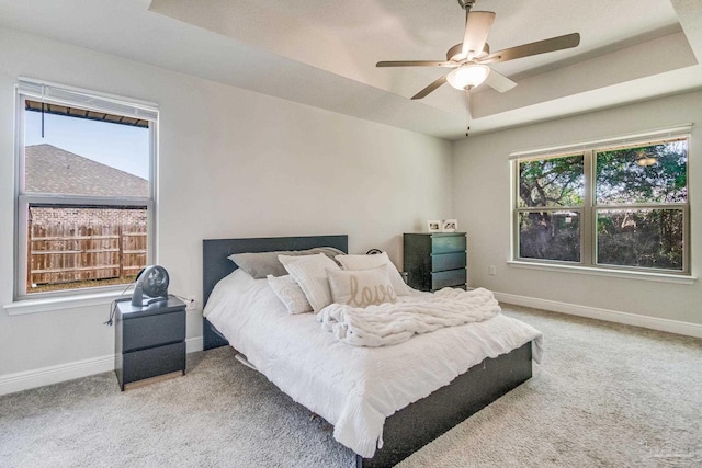 bedroom featuring light carpet, ceiling fan, multiple windows, and a tray ceiling