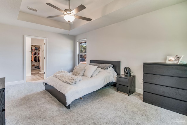 bedroom with a walk in closet, light carpet, a closet, a raised ceiling, and ceiling fan