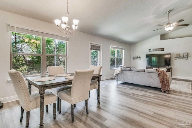 dining space with ceiling fan with notable chandelier, plenty of natural light, light wood-type flooring, and vaulted ceiling