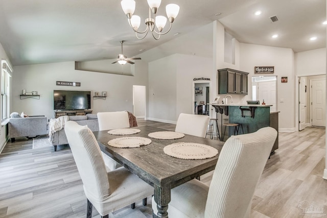 dining space featuring ceiling fan with notable chandelier, sink, high vaulted ceiling, and light wood-type flooring