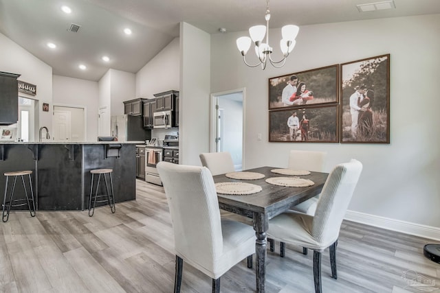 dining room with light wood-type flooring, a chandelier, high vaulted ceiling, and sink