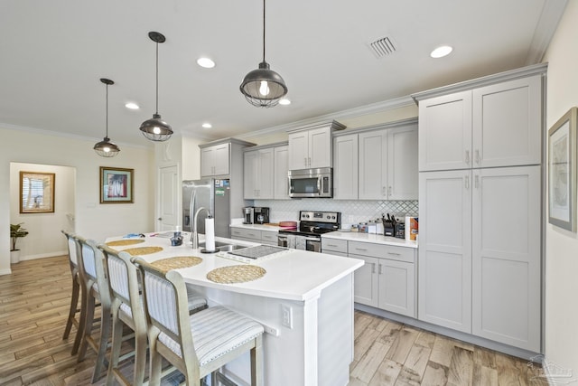 kitchen with stainless steel appliances, light countertops, visible vents, an island with sink, and a kitchen bar