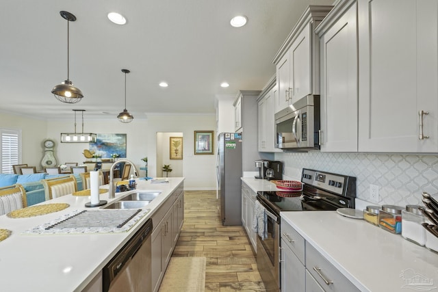 kitchen featuring light countertops, decorative backsplash, appliances with stainless steel finishes, a sink, and light wood-type flooring