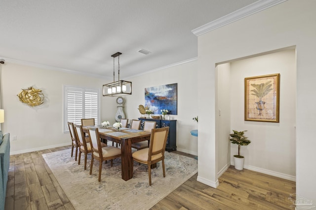 dining space with baseboards, visible vents, wood finished floors, and ornamental molding