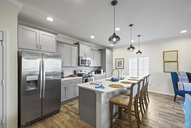 kitchen featuring crown molding, gray cabinets, light countertops, appliances with stainless steel finishes, and a sink