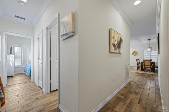 hall with wood finished floors, visible vents, and crown molding