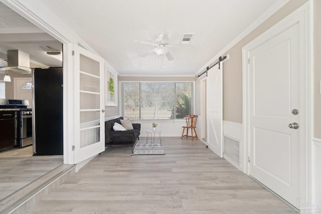 unfurnished room with ceiling fan, crown molding, light wood-type flooring, and a barn door